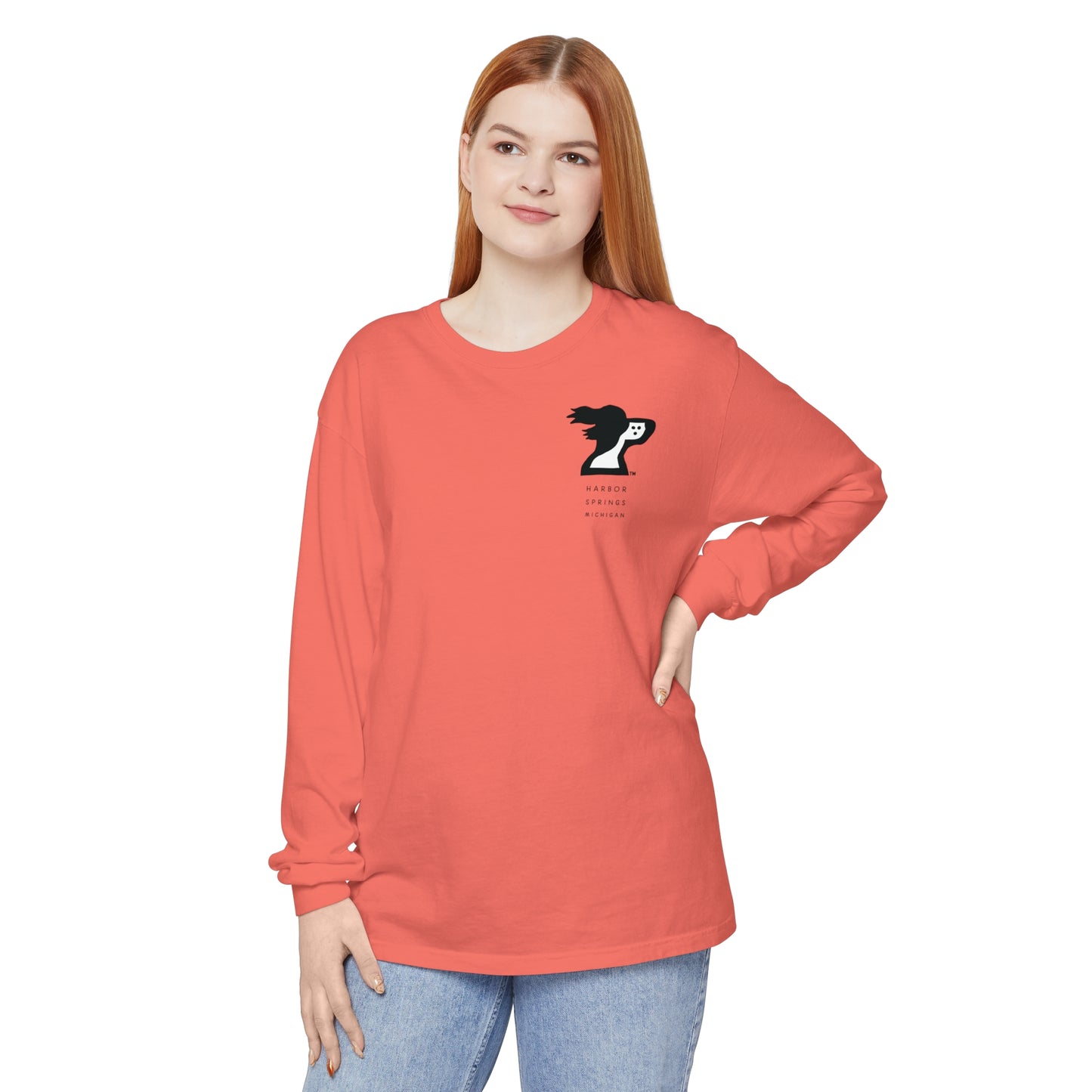 Woman wearing a salmon colored long sleeve t-shirt by the Harbor Springer brand with a springer spaniel dog logo and Harbor Springs Michigan text.