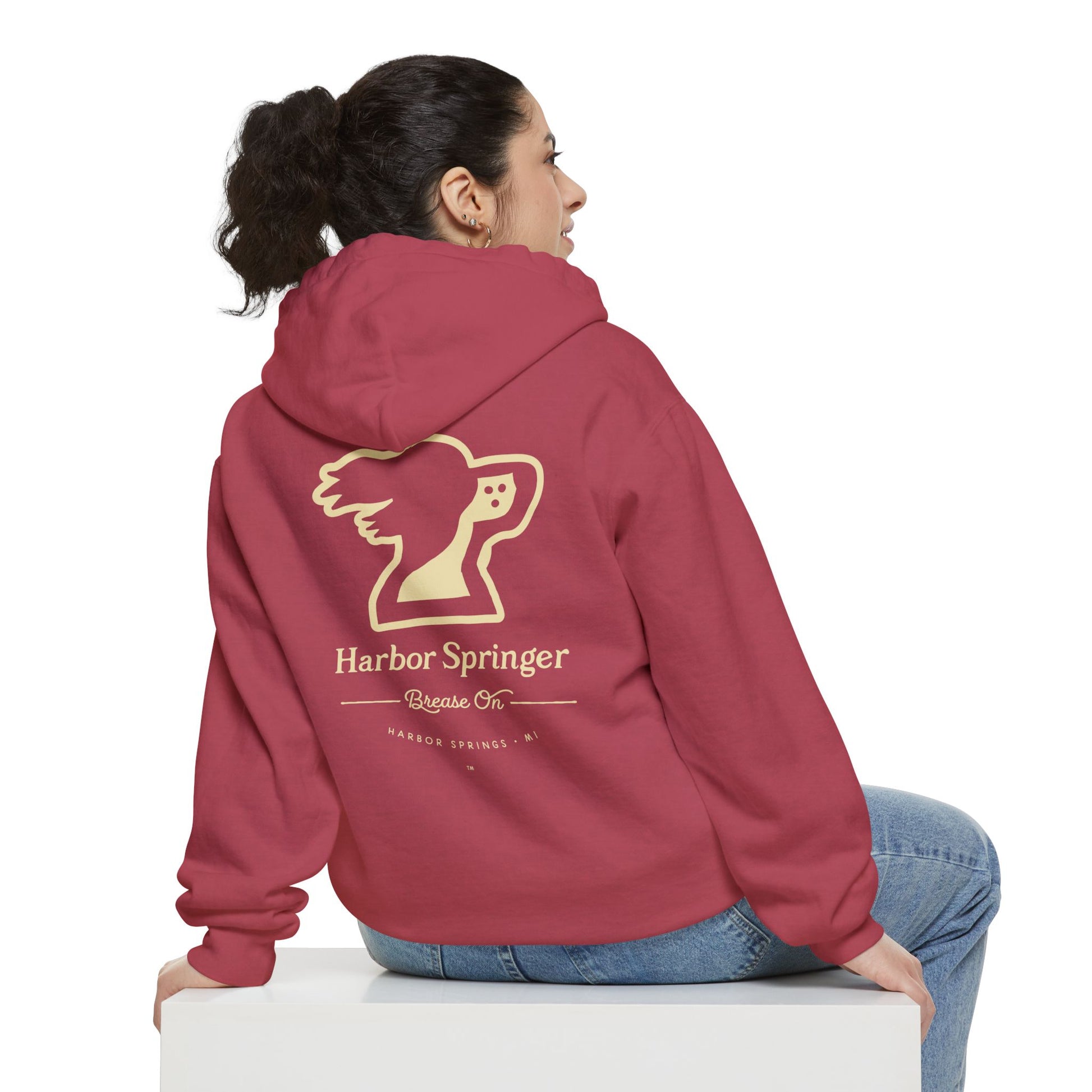 Woman sitting and wearing a red hoodie by the Harbor Springer brand with a springer spaniel dog logo and Brease On tagline on the back.