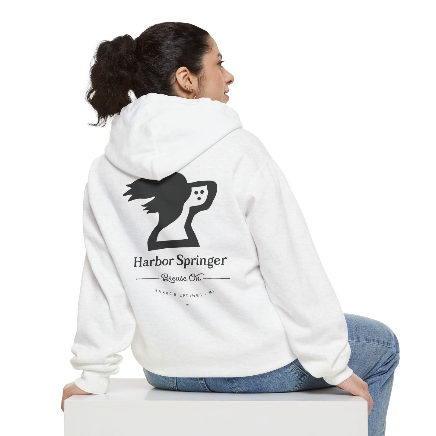 Woman sitting and wearing a white color hoodie by the Harbor Springer brand with a springer spaniel dog logo and Brease On tagline on the back.