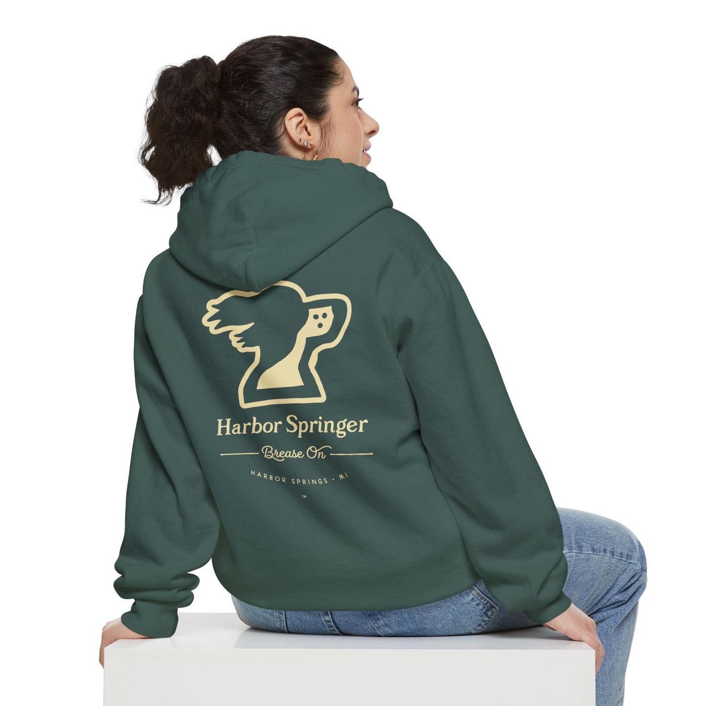 Woman sitting and wearing a green hoodie by the Harbor Springer brand with a springer spaniel dog logo and Brease On tagline on the back.