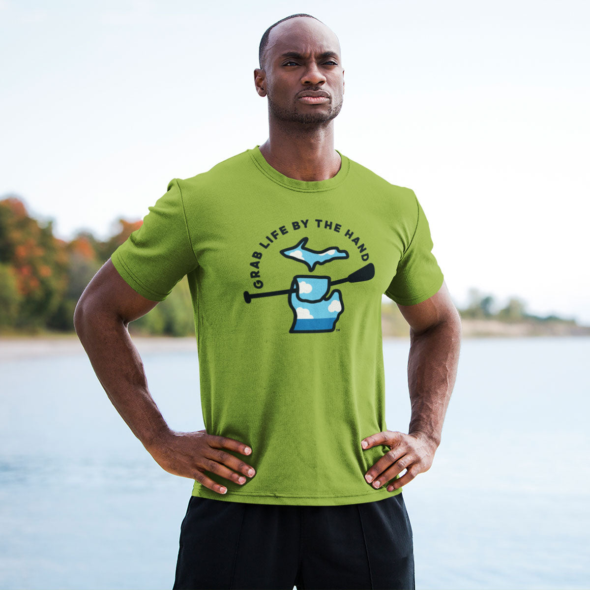 Man wearing a green Michigan t-shirt for people who kayak, canoe or paddleboard, showing the state of Michigan grabbing a paddle with the slogan Grab Life by the Hand™.