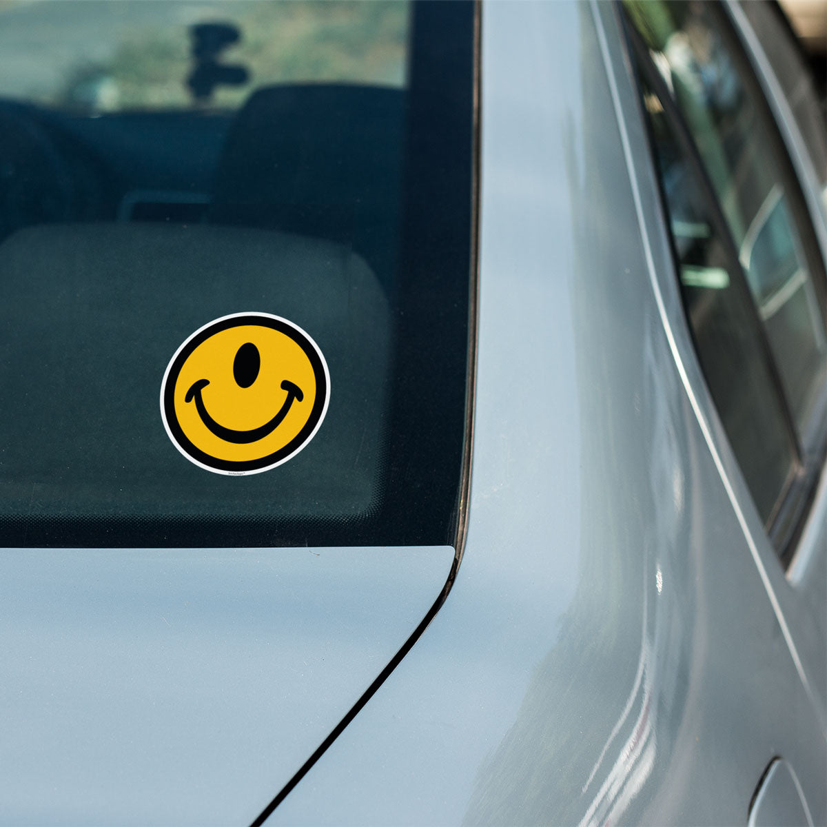 One-eyed smile face sticker that is indoor or outdoor on a car window by the Smileclops brand.