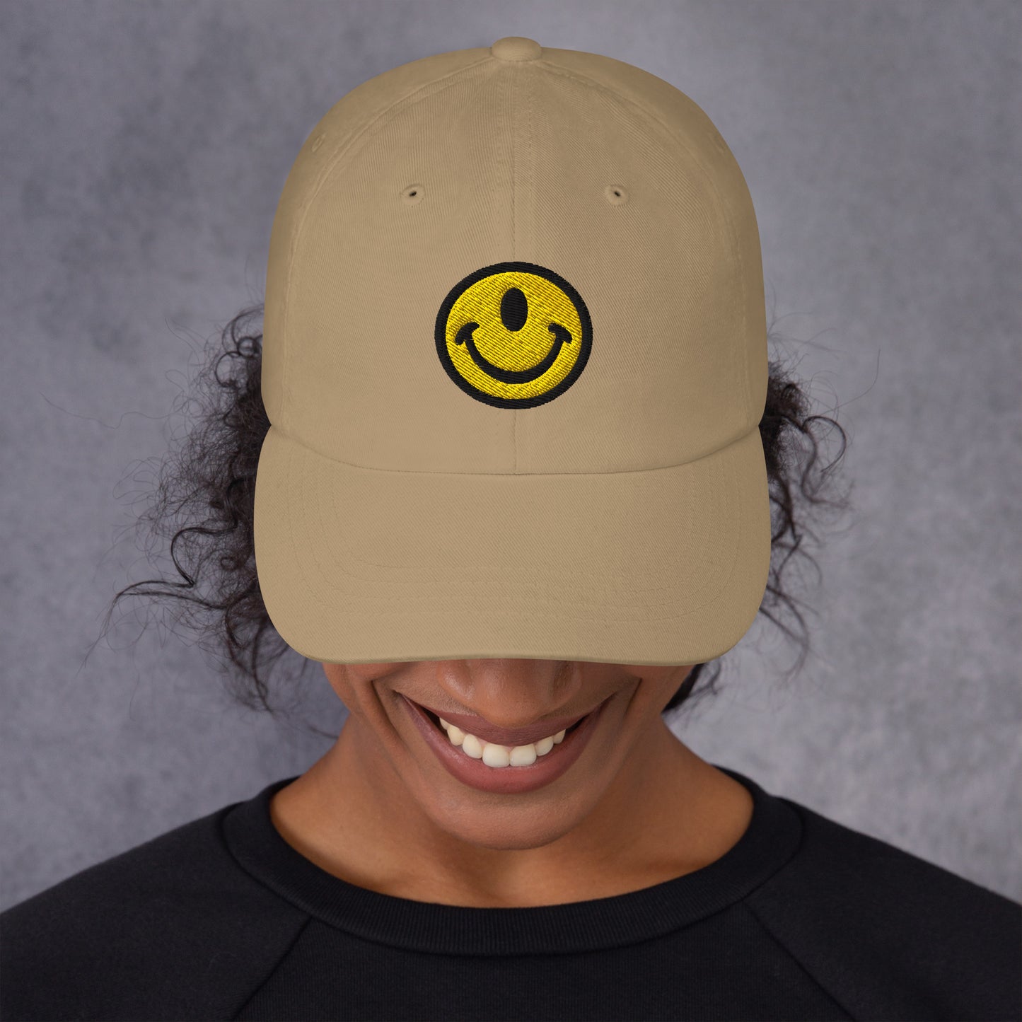 Woman wearing dad hat with the Smileclops™ brand logo of a one-eyed smile face, the official logo of resilient positivity for those who remain, in all things, Oddly Happy™.