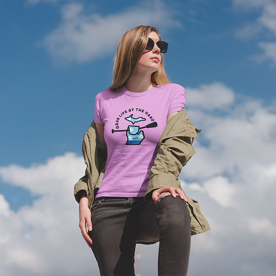 Woman wearing a pink Michigan tee that is for people who like kayaking, canoeing or paddleboarding, showing the state of Michigan grabbing a paddle with the slogan Grab Life by the Hand™.