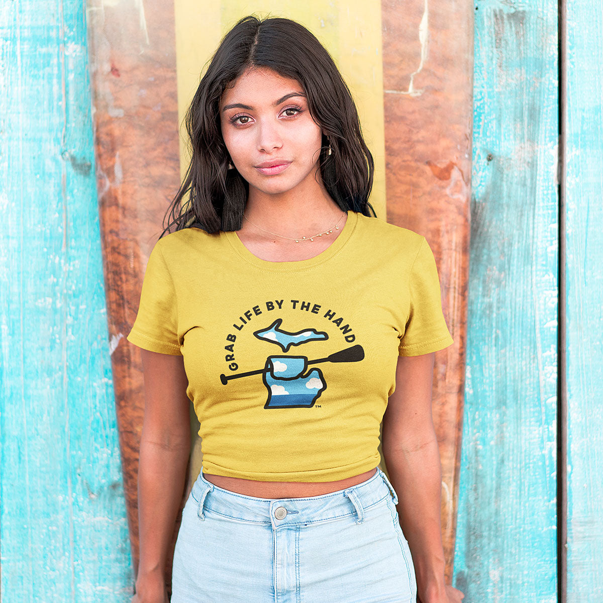 Woman wearing a yellow Michigan t-shirt for people who kayak, canoe or paddleboard, showing the state of Michigan holding a paddle with the slogan Grab Life by the Hand™.